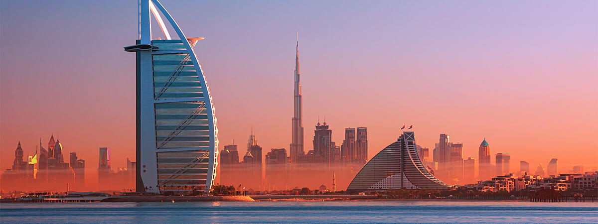 The famous buildings and skyline of dubai, as the sun sets pink over the water.