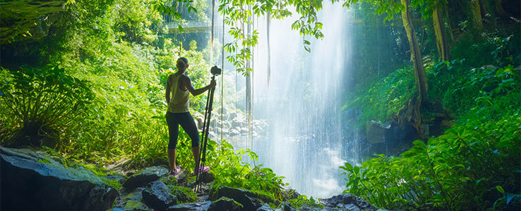A woman standing under Crystal Falls in the australian rainforest as part of an adventure holiday.