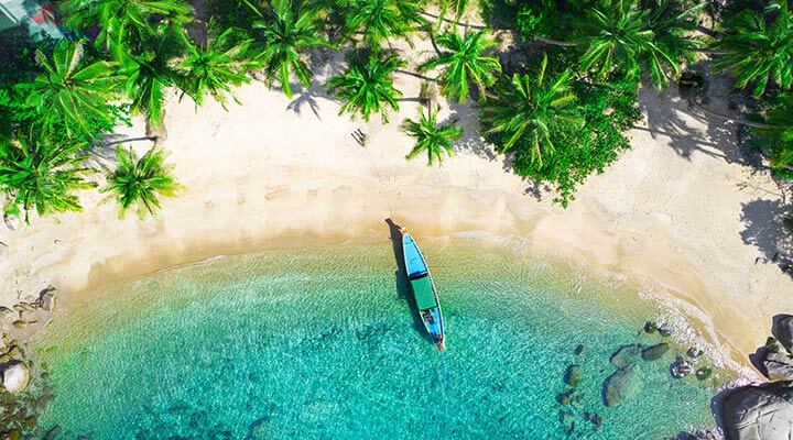 Aerial view of a longtail boat moored on a tropical beach on a private island in Thailand.