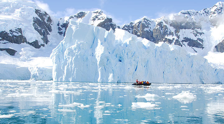 An antartic luxpedition cruise ship, in front of a glacier and icy lakes.