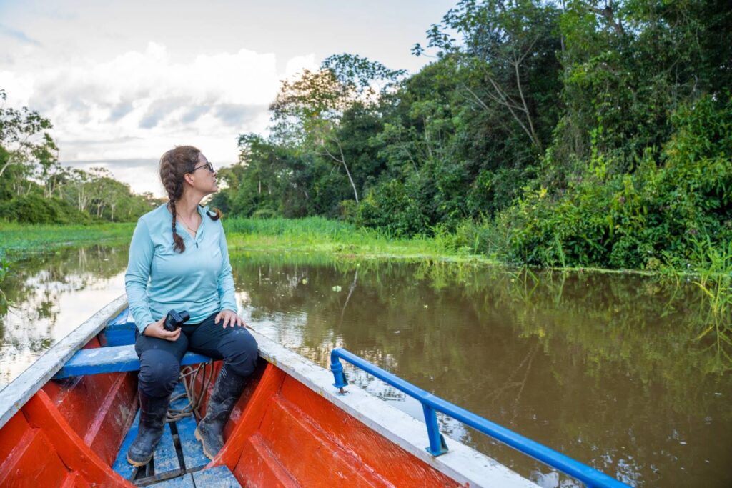 Woman wildlife watching from traditional wooden canoe on Amazon tributary, lush rainforest surrounds calm waters