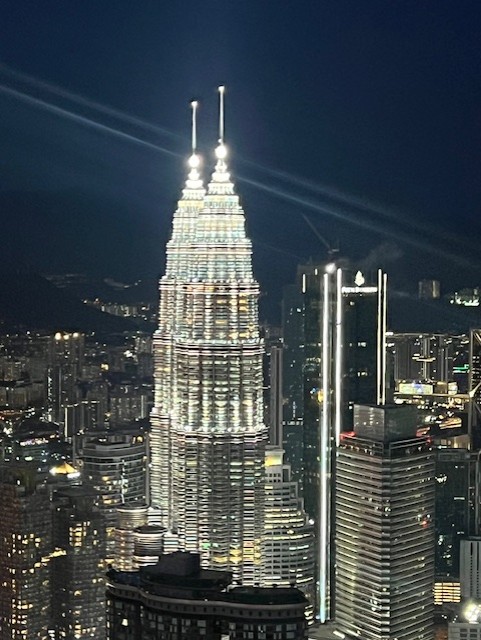 Petronas Twin Towers illuminated at night in Kuala Lumpur, glowing silver against dark sky with surrounding skyscrapers