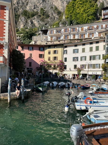 Colorful Italian buildings and harbor with boats in Lake Garda lakeside town, dramatic mountain cliffs backdrop, cafes and shops showcasing charming Italy lake escapes and Lake Garda holidays